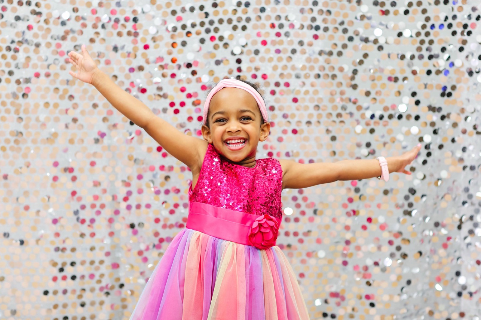 Yohanna in a sparkly pink party dress with arms wide open