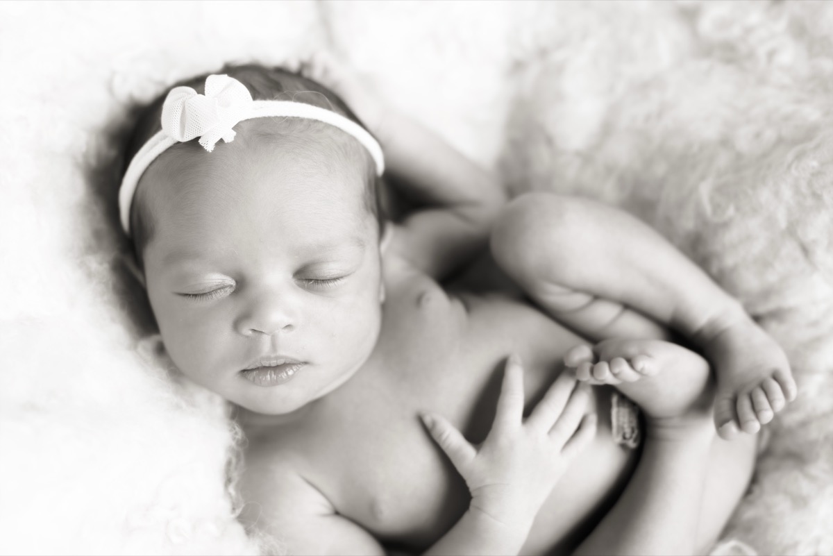 Newborn Yohanna sleeping peacefully on a soft white blanket with a delicate bow headband
