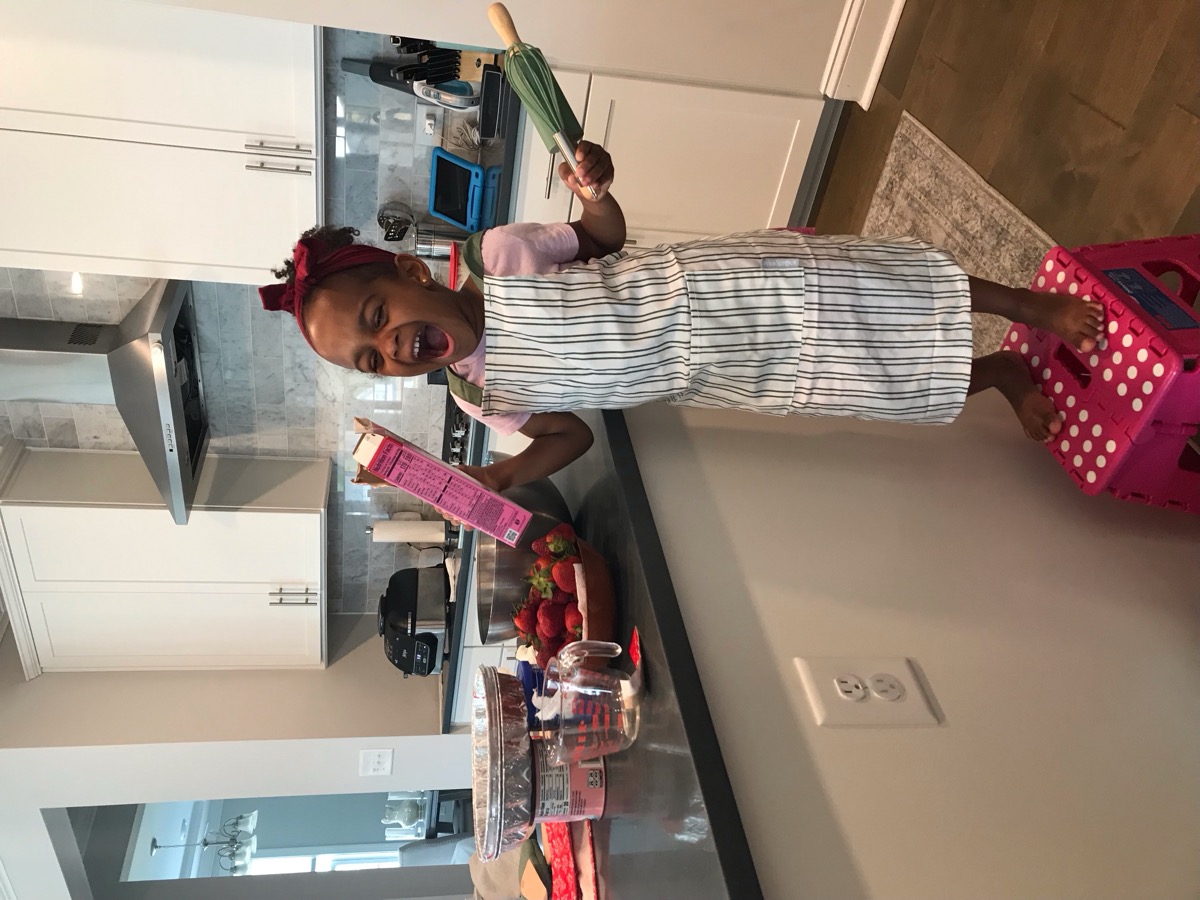 Yohanna in a striped apron baking in the kitchen, holding a rolling pin and laughing with joy