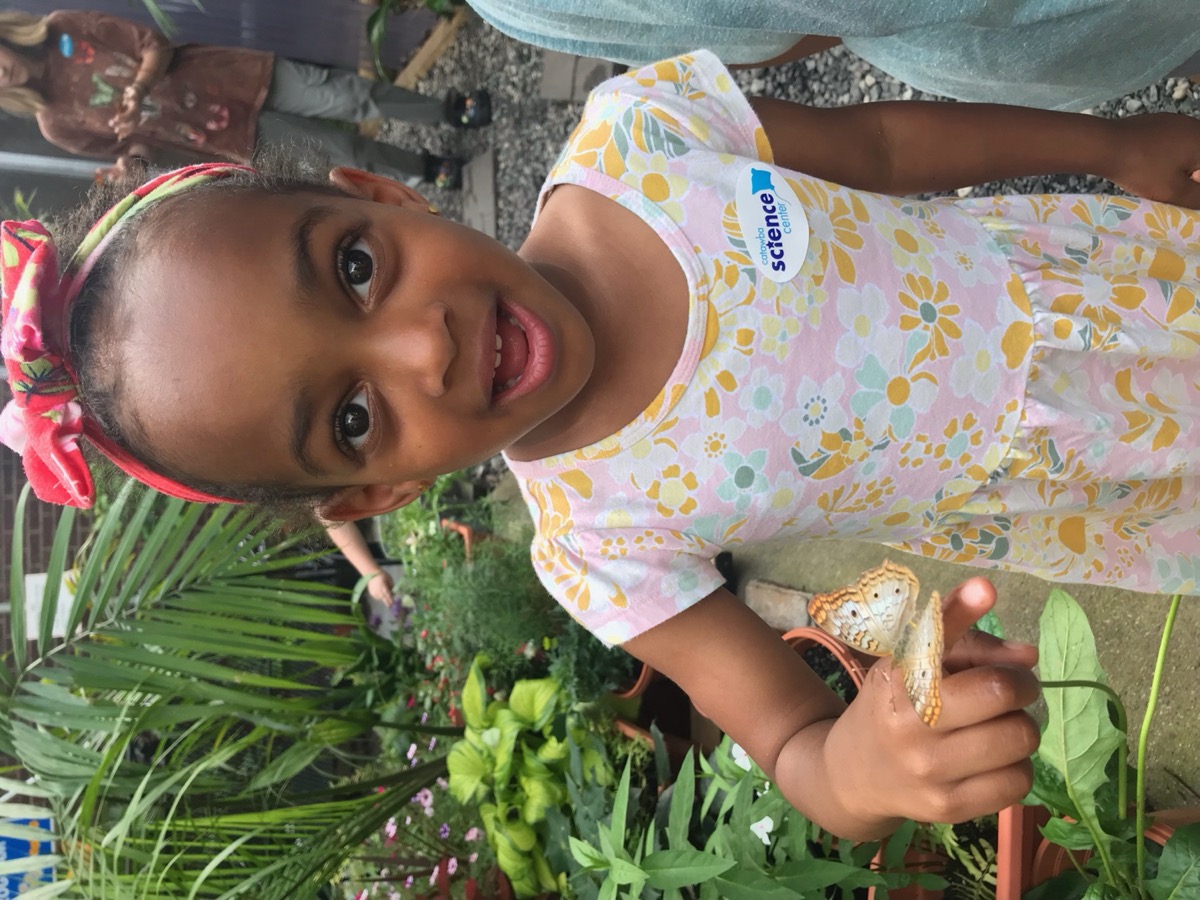 Yohanna at the Catawba Science Center butterfly garden, holding a butterfly on her finger with wide eyes