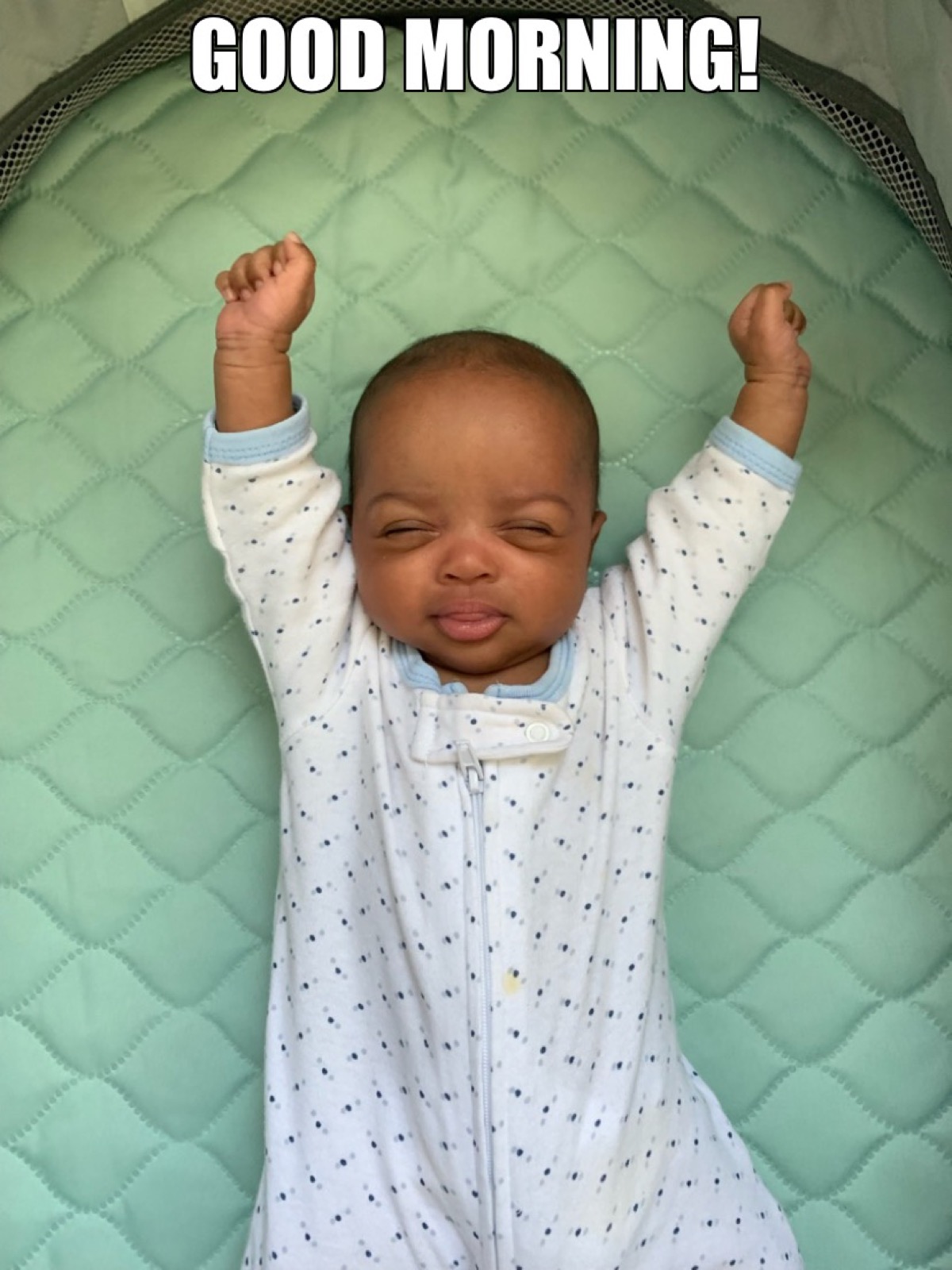 Baby Yohanna stretching with arms raised in a polka-dot onesie on a green quilted mat, captioned Good Morning