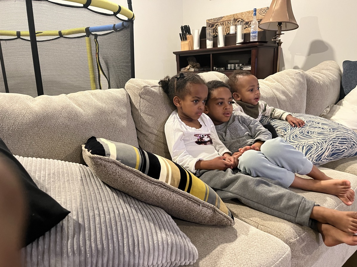 Yohanna, her older brother, and twin brother cuddled on the couch watching a show together in cozy clothes