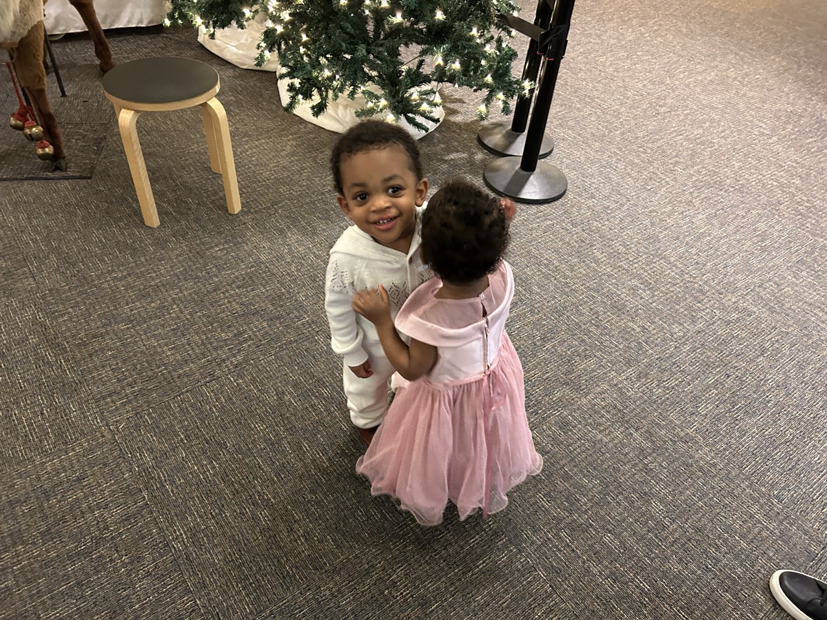 Yohanna and her twin brother dancing together near the Christmas tree — she is in a pink tutu and he is in a white sparkle hoodie