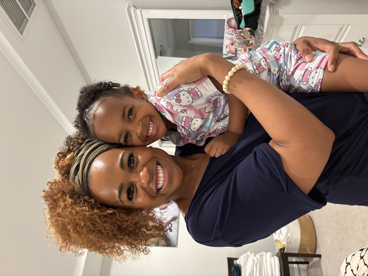 Yohanna being held by a woman with curly auburn hair and an olive headband — Yohanna in Hello Kitty pajamas, both smiling warmly