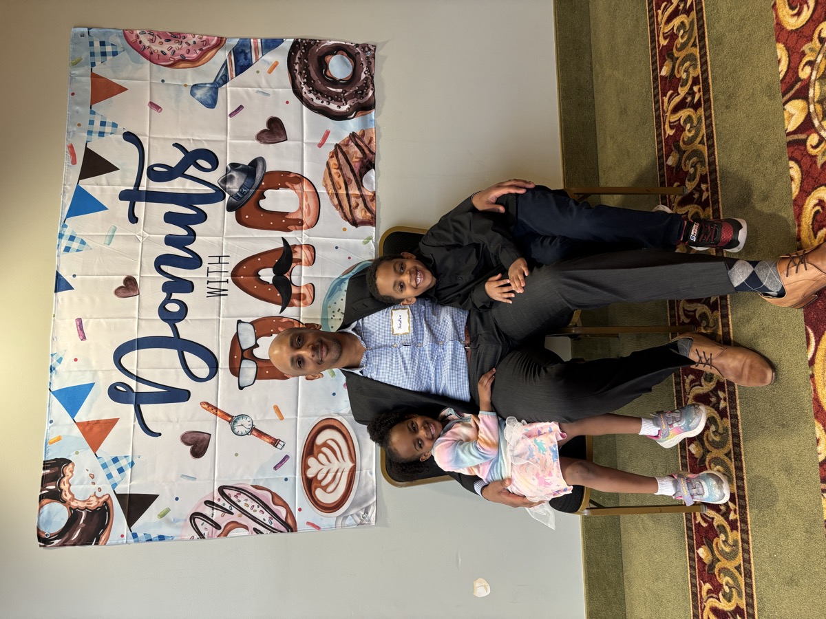Dad with Yohanna and her older brother at a Donuts with Dad event — Yohanna in a pastel jacket, her brother in a black button-down