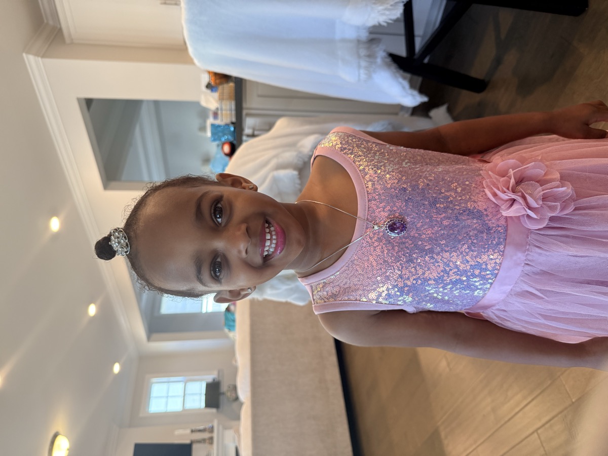 Yohanna smiling big in a pink sequin gradient dress with a tulle skirt, tiara hair clip, and a purple gemstone necklace